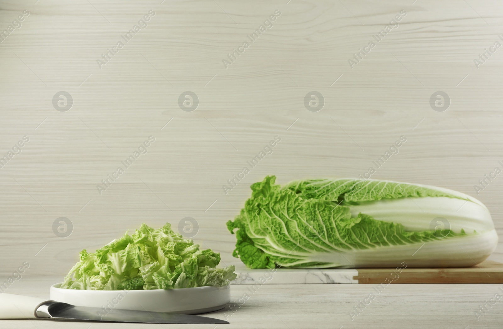 Photo of Whole and cut fresh ripe Chinese cabbage on table against white wooden background. Space for text