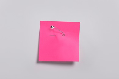 Pink paper note attached with safety pin to white background, top view