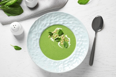 Photo of Plate of healthy green soup with fresh spinach served on white wooden table, flat lay