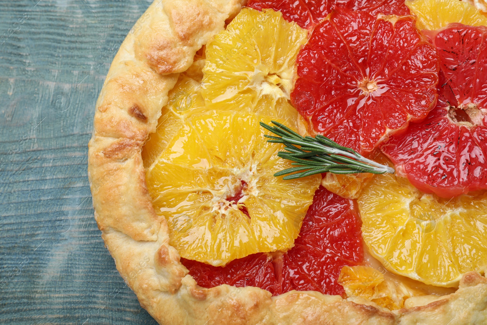 Photo of Delicious galette with citrus fruits and rosemary on blue wooden table, top view