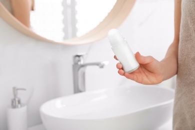 Young woman with roll on deodorant in bathroom, closeup view. Space for text