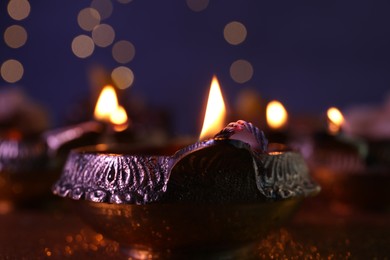 Photo of Diwali celebration. Diya lamp on table against blurred lights, closeup