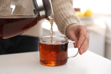 Photo of Woman pouring hot tea into cup at white table, closeup