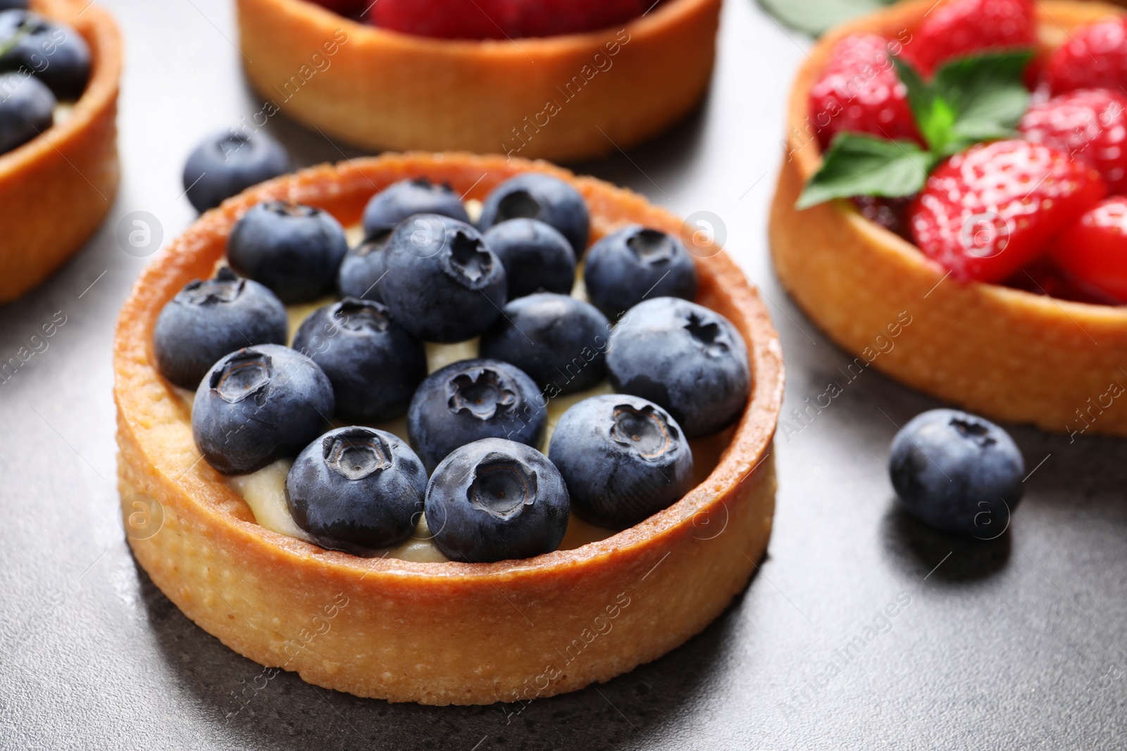 Photo of Tartlet with fresh blueberries on grey table, closeup. Delicious dessert