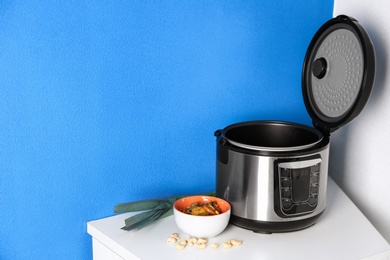 Modern multi cooker and ingredients on table near color wall, space for text