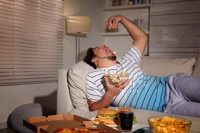 Photo of Overweight man with bowl of popcorn on sofa at home