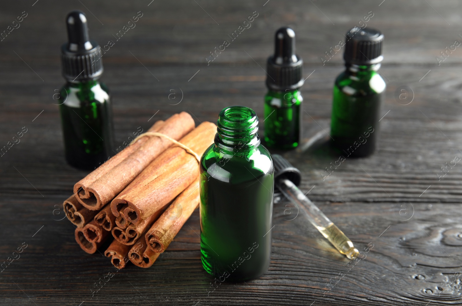 Photo of Bottles with essential oil and cinnamon sticks on black wooden table