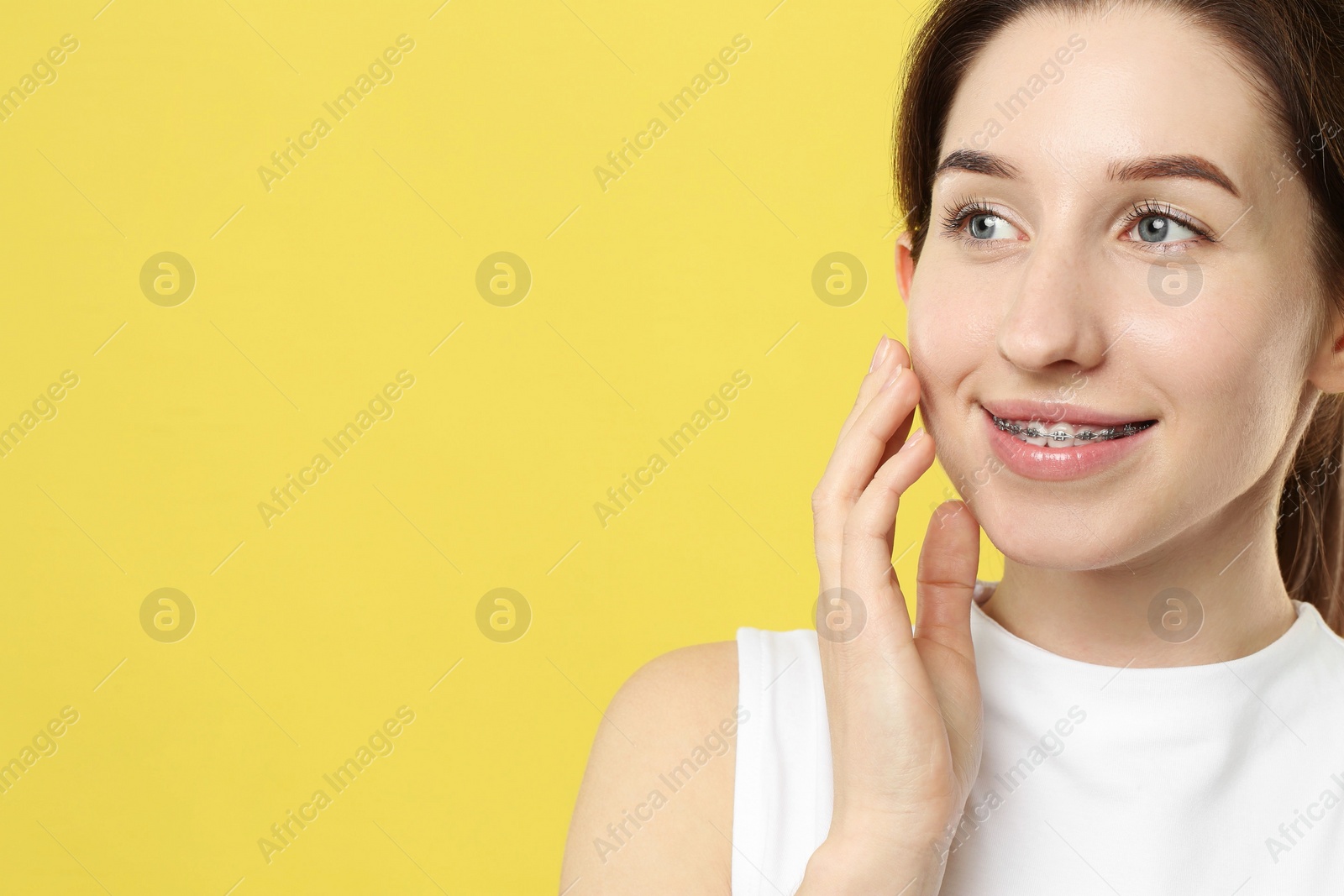 Photo of Portrait of smiling woman with dental braces on yellow background. Space for text