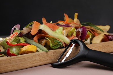 Peels of fresh vegetables and peeler on dusty pink background, closeup