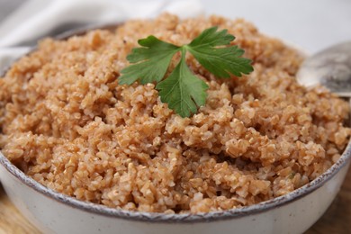 Photo of Tasty wheat porridge with parsley in bowl on table, closeup