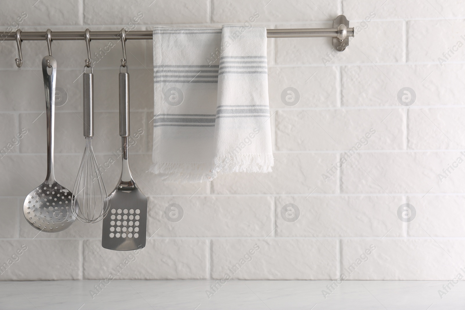 Photo of Soft kitchen towel and utensils hanging on rack near white brick wall