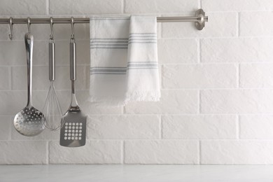 Photo of Soft kitchen towel and utensils hanging on rack near white brick wall