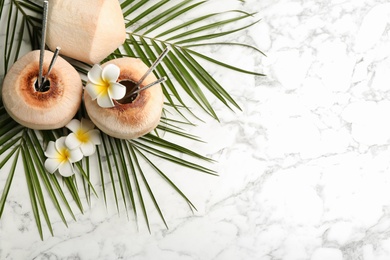 Photo of Fresh coconut with drinking straws and flowers on white marble table, flat lay. Space for text