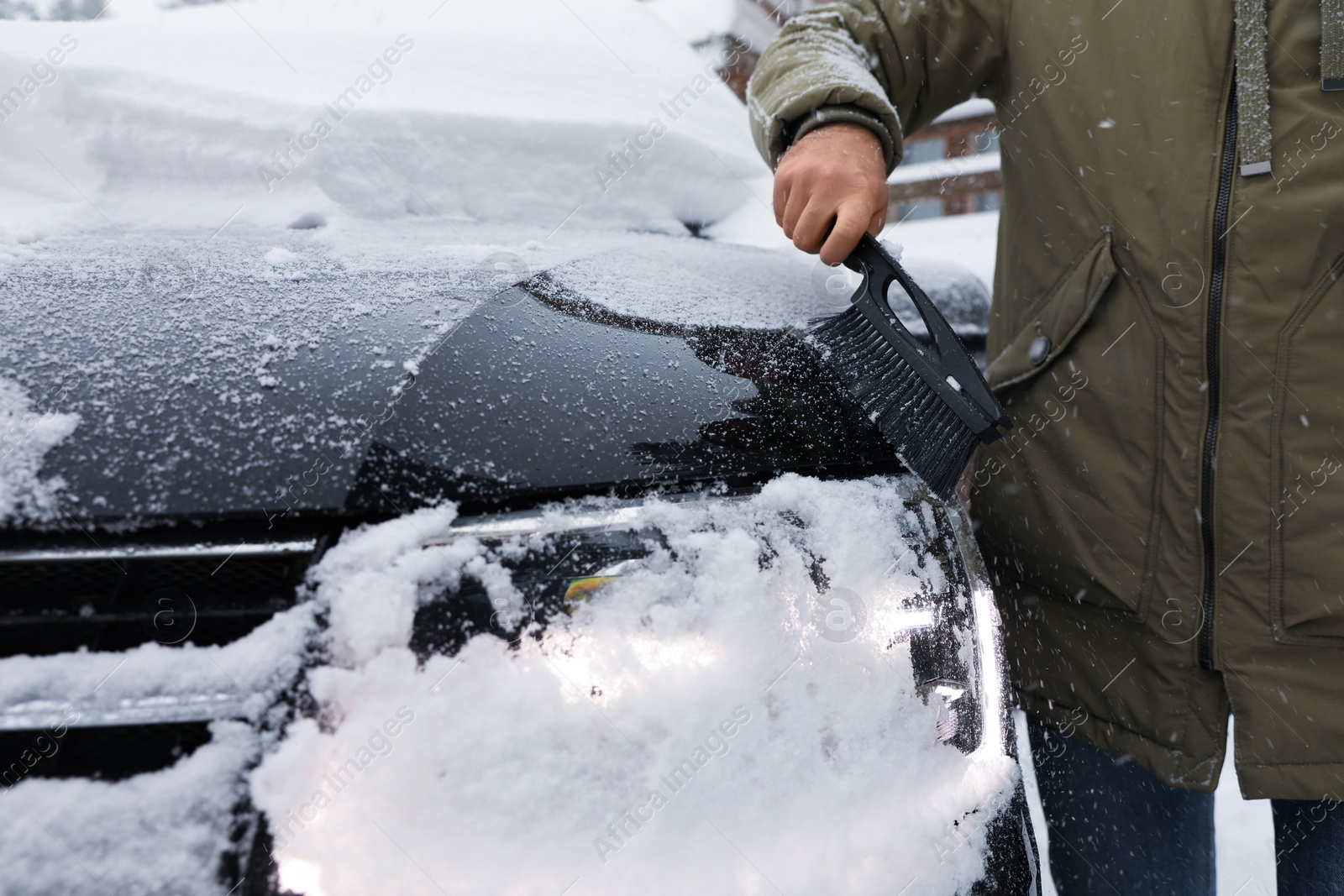 Photo of Young man cleaning snow from car outdoors on winter day, closeup