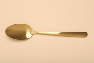 One shiny golden spoon on beige background, top view