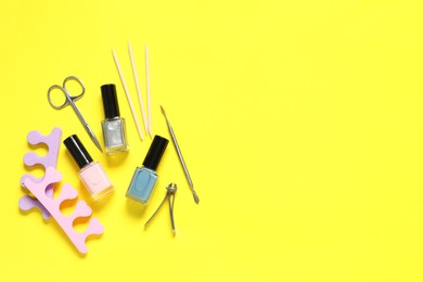 Nail polishes and set of pedicure tools on yellow background, flat lay. Space for text