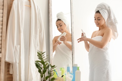 Photo of Young woman applying body cream near mirror in bathroom