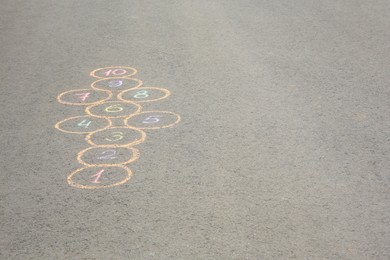 Hopscotch drawn with colorful chalk on asphalt outdoors, space for text