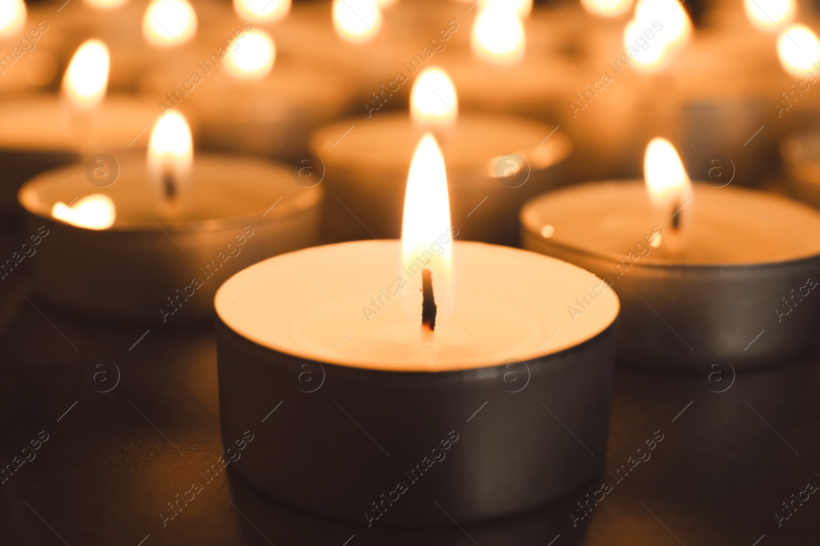 Photo of Burning candles on table in darkness, closeup. Funeral symbol