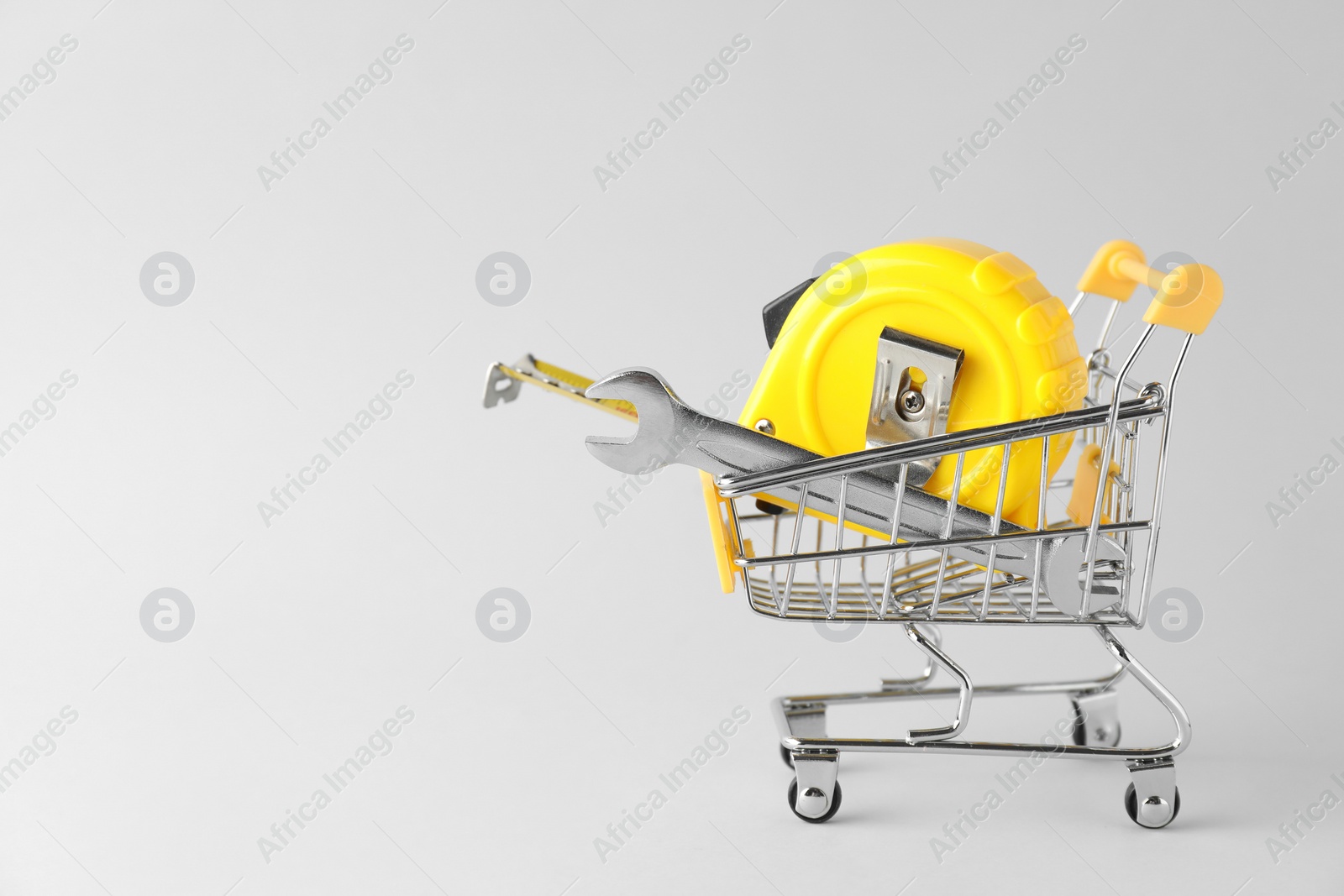 Photo of Metal wrench and measuring tape in shopping cart on light grey background, space for text