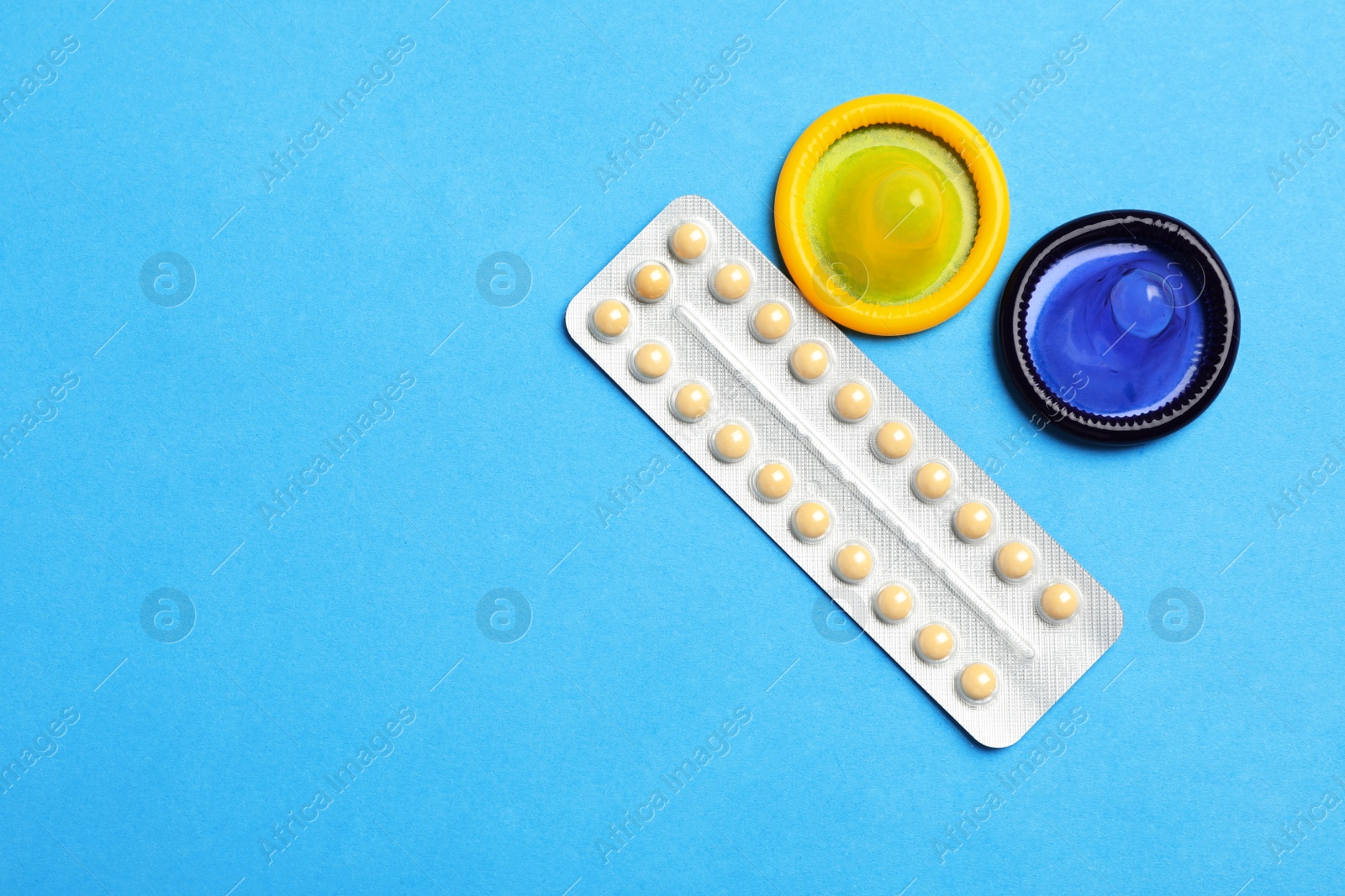 Photo of Condoms and birth control pills on light blue background, flat lay with space for text. Safe sex concept