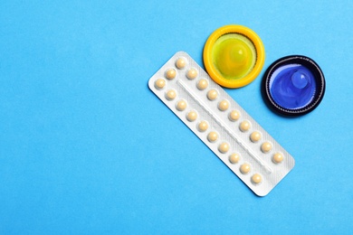 Photo of Condoms and birth control pills on light blue background, flat lay with space for text. Safe sex concept