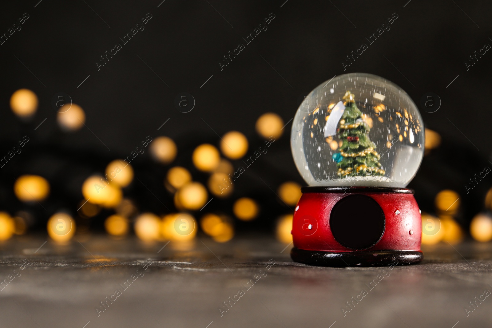 Photo of Snow globe with Christmas tree on grey table against festive lights, space for text