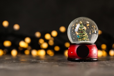 Snow globe with Christmas tree on grey table against festive lights, space for text