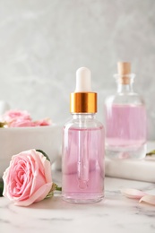 Bottle of essential oil and rose on marble table