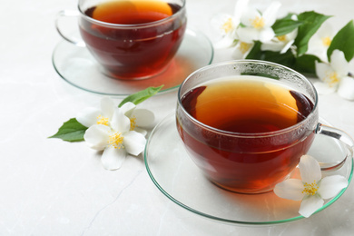 Cups of tea and fresh jasmine flowers on light grey marble table