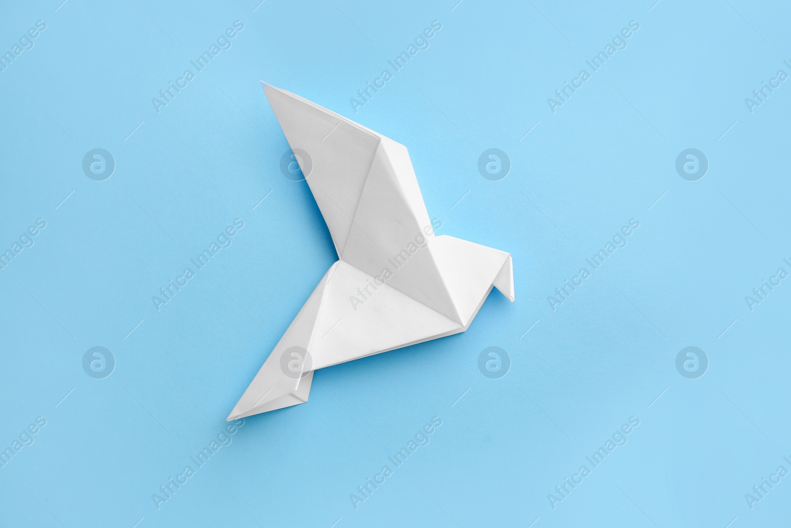 Photo of Origami art. Beautiful handmade paper bird on light blue background, top view