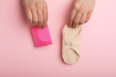 Photo of Woman holding disposable and reusable cloth menstrual pads on pink background, top view