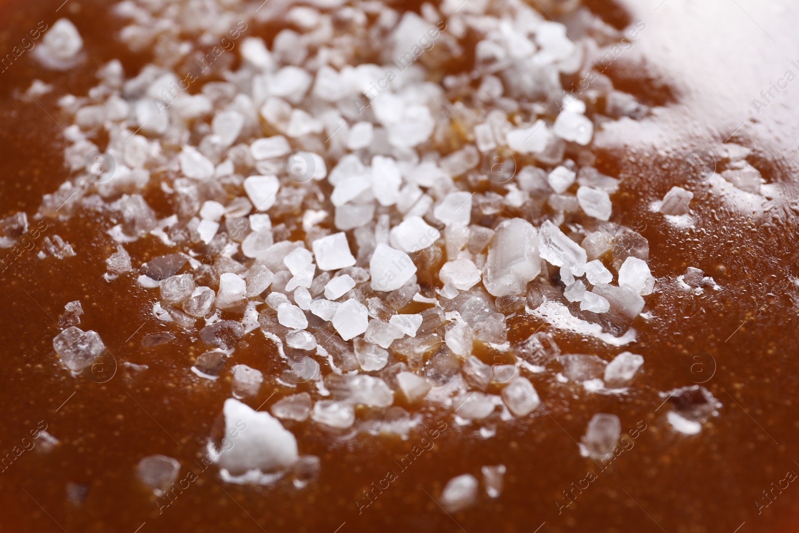 Photo of Delicious caramel sauce with sea salt as background, closeup