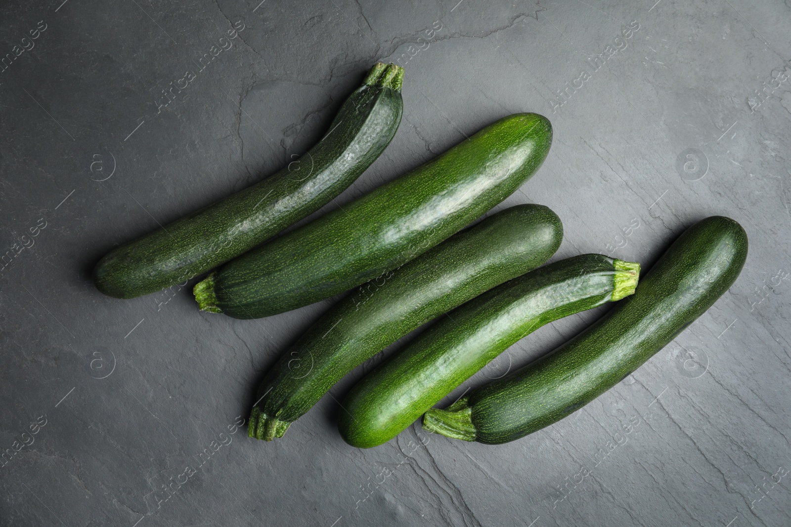 Photo of Green ripe zucchinis on black slate table, flat lay