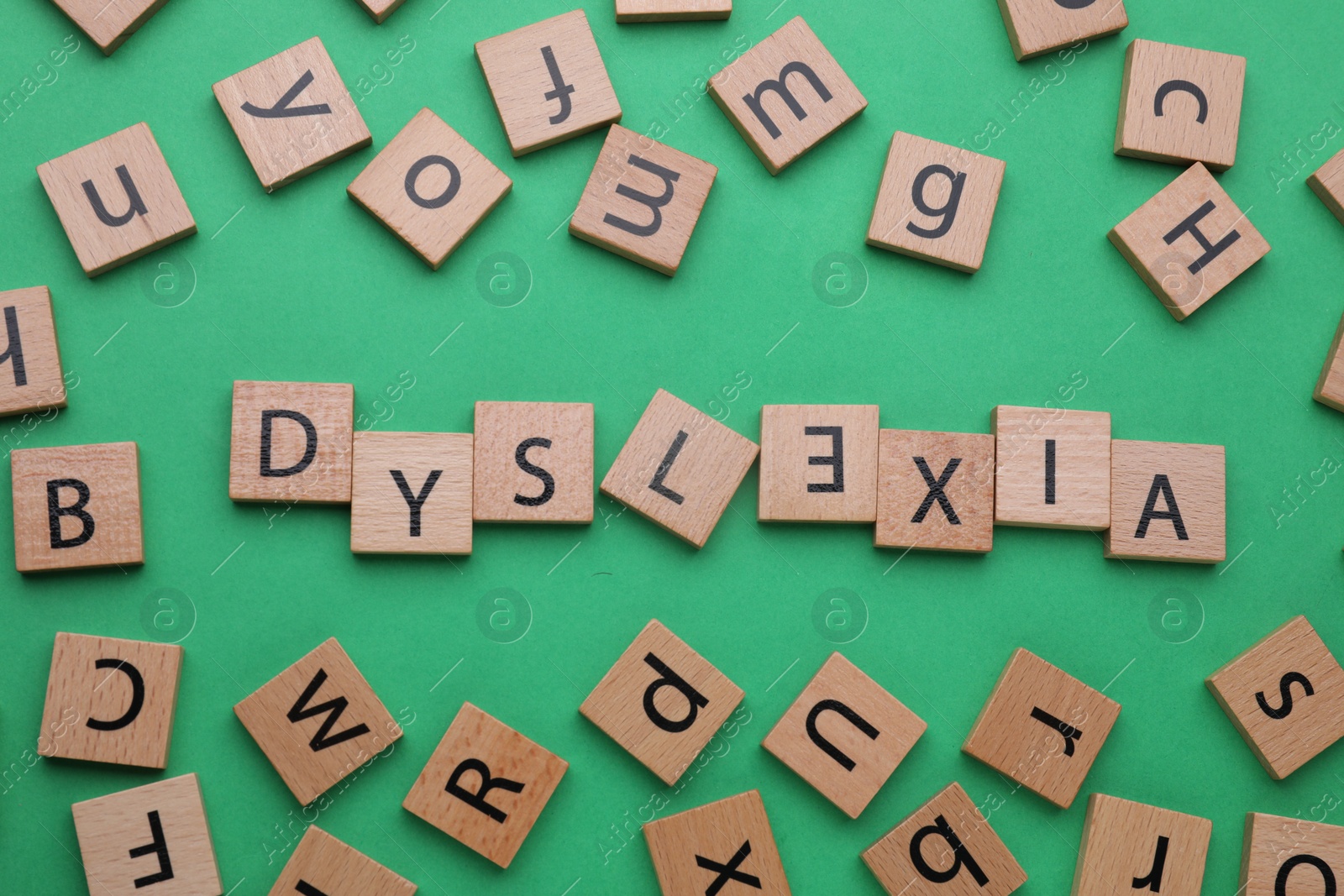 Photo of Word Dyslexia with inverted letter E of wooden tiles on green background, flat lay