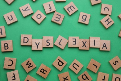 Photo of Word Dyslexia with inverted letter E of wooden tiles on green background, flat lay