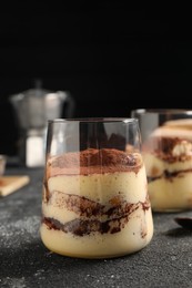 Photo of Delicious tiramisu in glasses on grey textured table