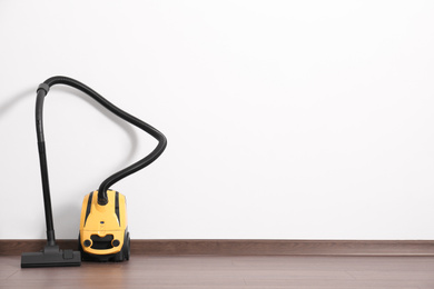 Modern yellow vacuum cleaner on wooden floor near white wall, space for text