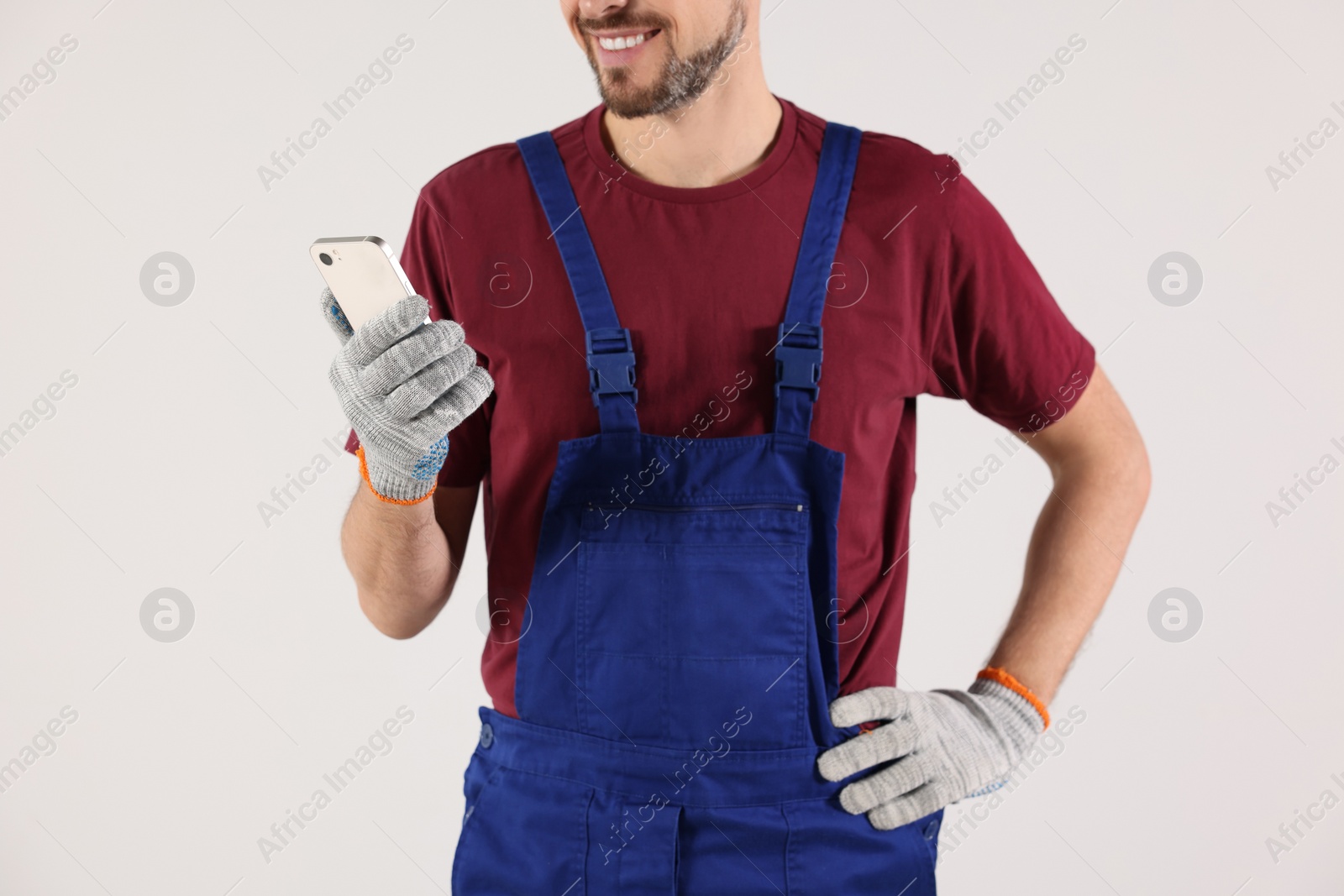 Photo of Professional repairman in uniform with phone indoors, closeup