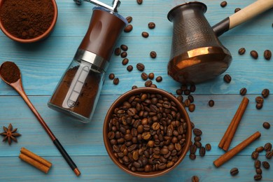 Photo of Manual coffee grinder with powder, beans and jezve on light blue wooden table, flat lay