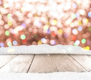 Image of Wooden surface with heap of snow and blurred Christmas lights on background, bokeh effect 