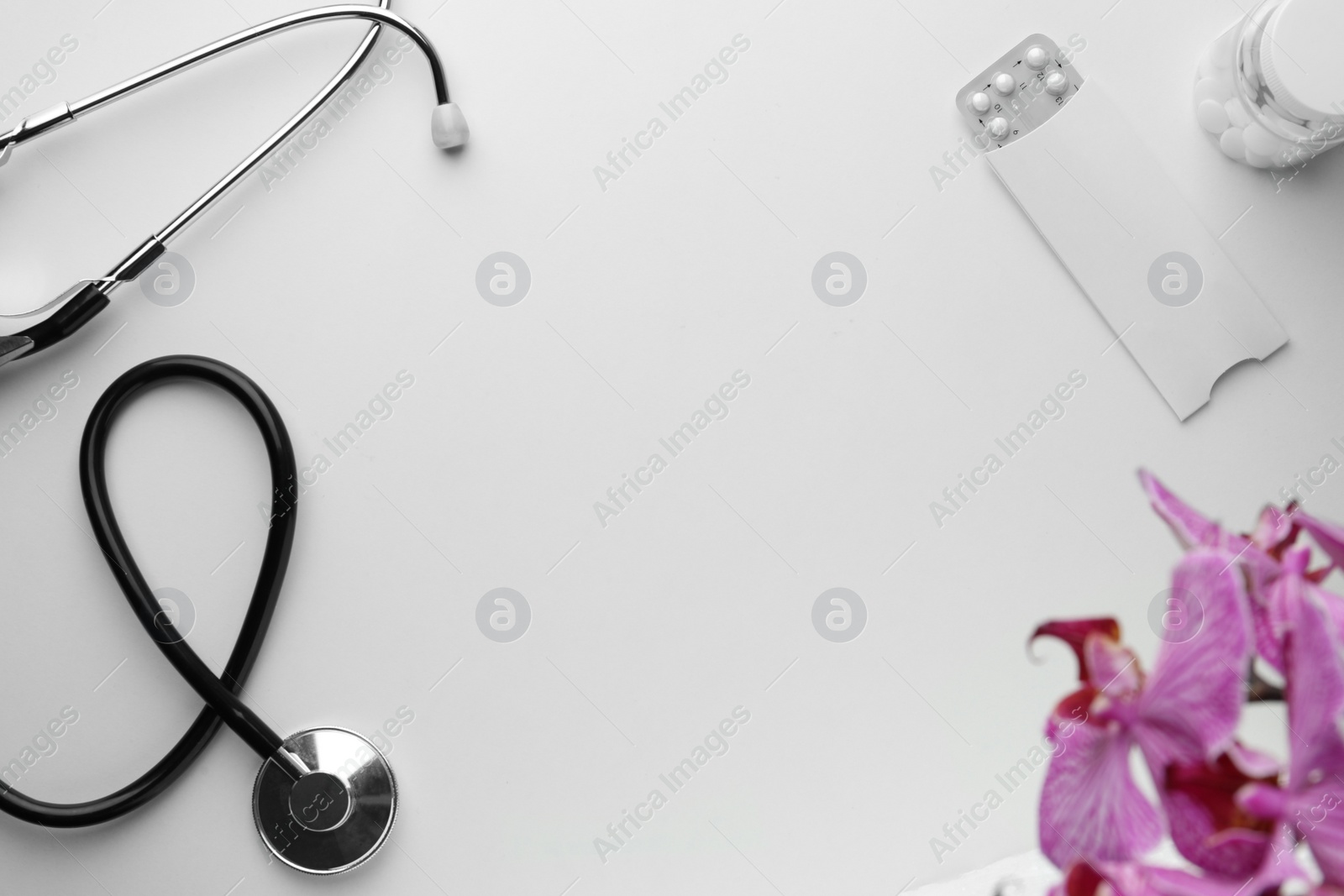 Photo of Stethoscope, pills and orchid flower on white background, flat lay with space for text. Women's Health concept