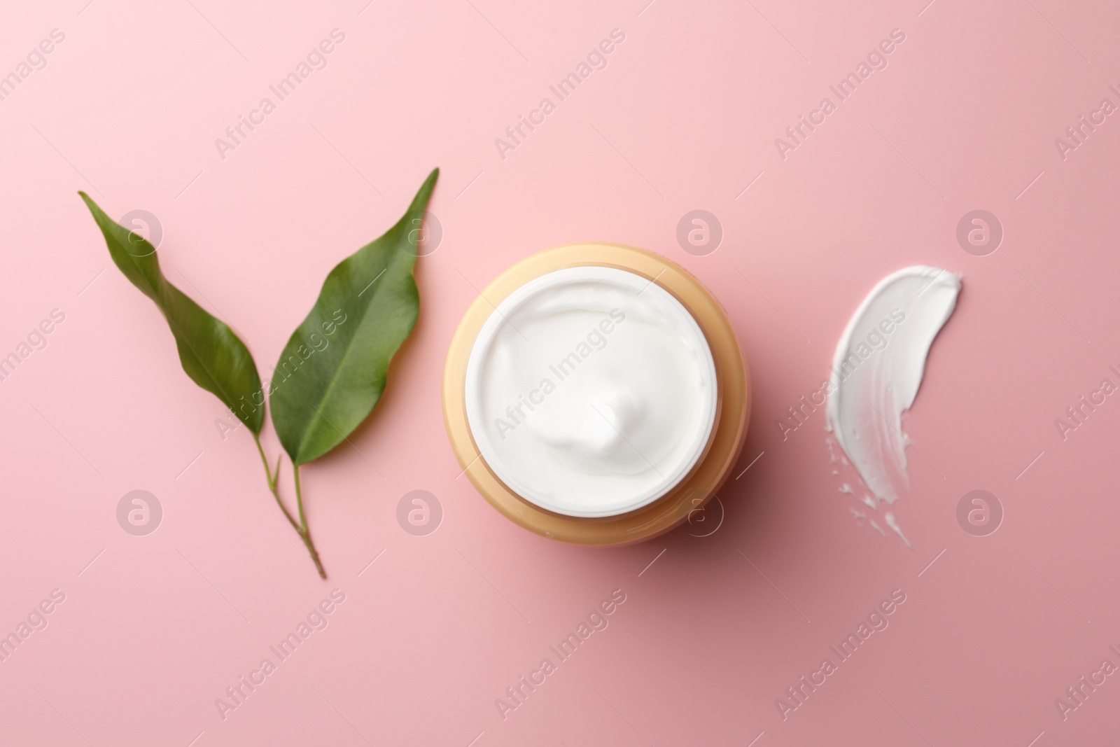 Photo of Jar of face cream, sample and fresh leaves on pink background, flat lay
