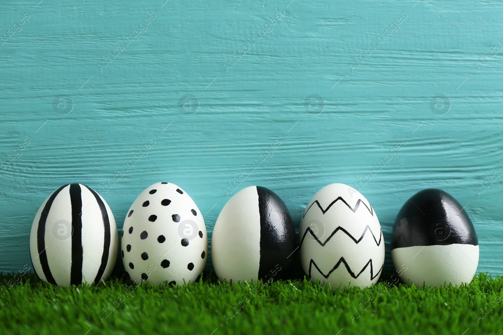 Photo of Line of painted Easter eggs on green lawn against wooden background, space for text