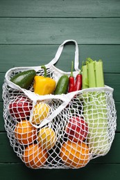 Photo of String bag with different vegetables on green wooden table, top view