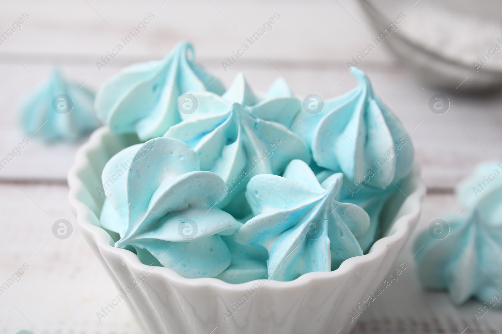 Photo of Tasty meringue cookies in bowl on white wooden table, closeup