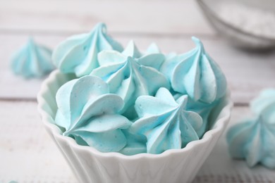 Photo of Tasty meringue cookies in bowl on white wooden table, closeup