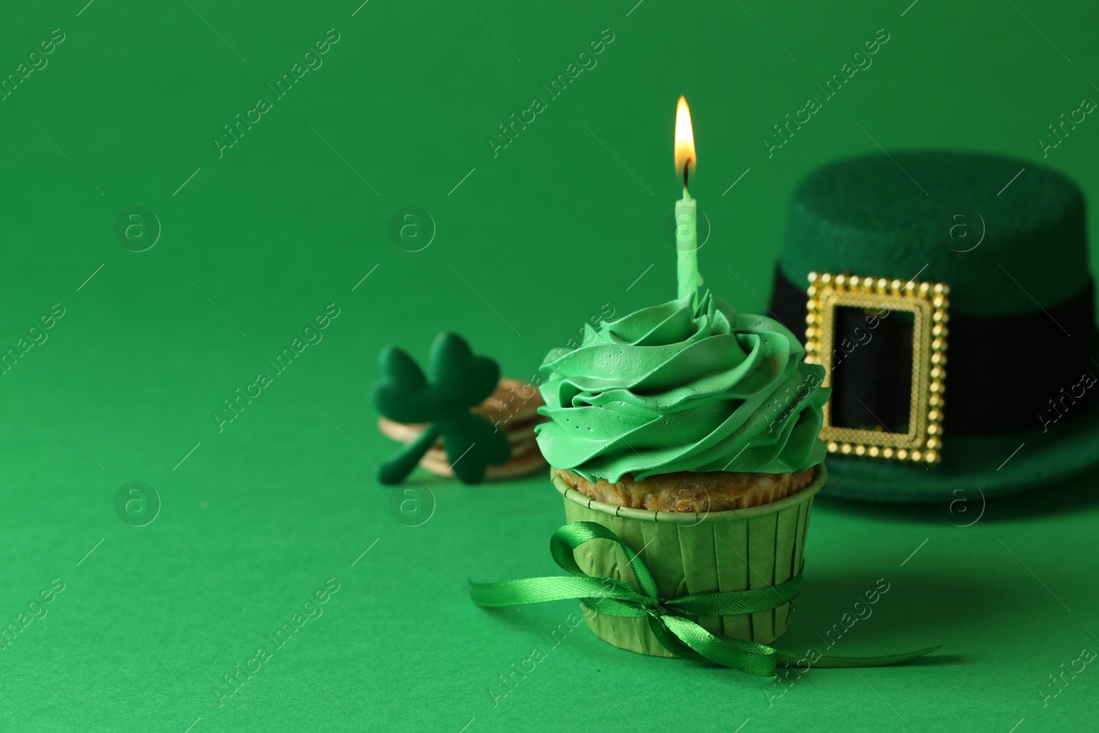 Photo of St. Patrick's day party. Tasty cupcake with burning candle and leprechaun hat on green background. Space for text