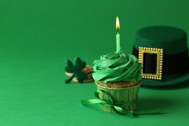 St. Patrick's day party. Tasty cupcake with burning candle and leprechaun hat on green background. Space for text