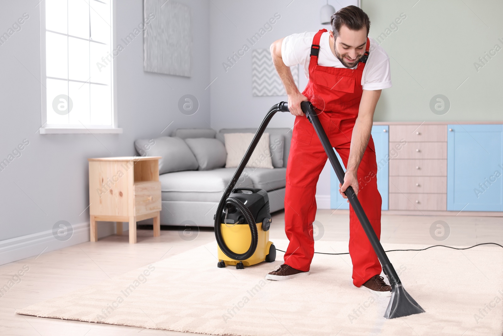 Photo of Male worker cleaning carpet with vacuum in living room